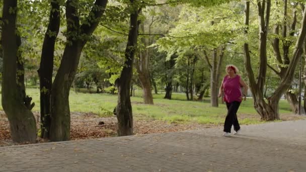 Äldre gumman springer i parken och använder smart klocka. Kvinnlig löpare tränar cardio utomhus — Stockvideo