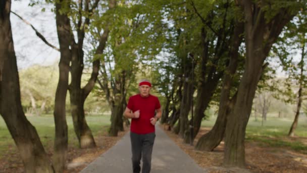 Male senior person running along road in park, using smart watch, tracking result fitness workout