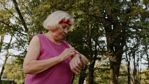 Senior mulher corredor esporte usando relógio inteligente tocando touchscreen, resultado de rastreamento. Exercício de fitness — Fotografia de Stock