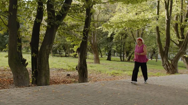 Старша стара жінка бігає в парку і використовує розумний годинник. Жіночий бігун, що розробляє кардіо на відкритому повітрі — стокове фото