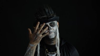 Korkunç cadılar bayramı makyajlı ürkütücü adam yüzünü asıyor, elinin arkasına saklanıyor.