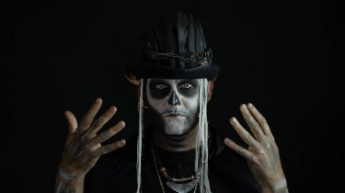 Korkunç cadılar bayramı makyajlı ürkütücü adam yüzünü asıyor, elinin arkasına saklanıyor.