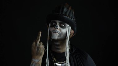 Kafatası makyajlı, suratını buruşturan ve orta parmağını gösteren uğursuz bir adam. Kötü bir jest. Cadılar Bayramı