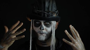 Korkunç cadılar bayramı makyajlı ürkütücü adam yüzünü asıyor, elinin arkasına saklanıyor.