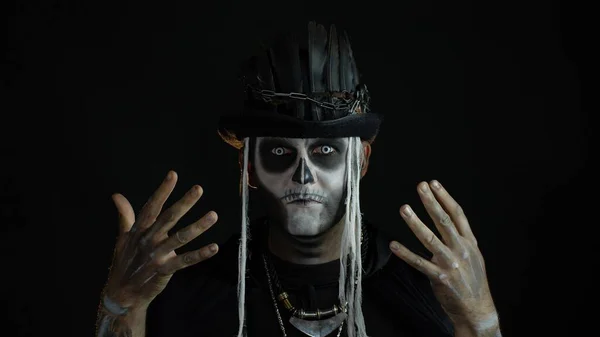 Przerażający mężczyzna z okropnym halloween szkieletowym makijażem robi miny, chowa się za ręką — Zdjęcie stockowe