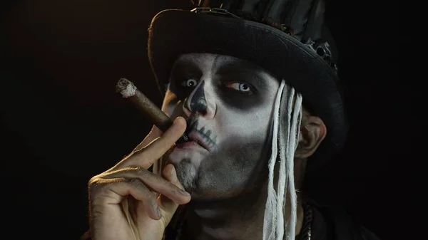 Зловещий человек с ужасным скелетом на Хэллоуин поднимает голову и курит сигару — стоковое фото