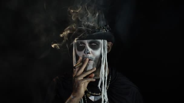 Sinistere man met afschuwelijke Halloween skelet make-up roken sigaar, gezicht trekken, kijken naar de camera — Stockvideo