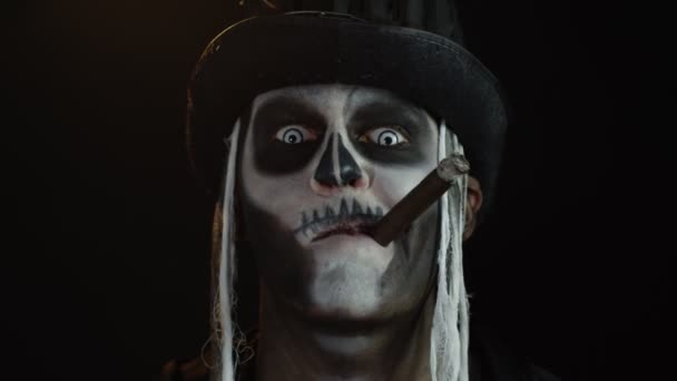Синістер з жахливим скелетним макіяжем на Хеллоуїн курить сигару, робить обличчя, посміхається, сміється — стокове відео