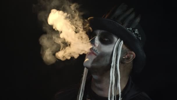Hombre siniestro con maquillaje de cráneo profesional exhalando humo de cigarrillo de su boca y nariz — Vídeo de stock