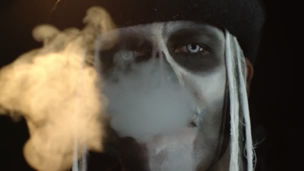 Portrait of scary guy in thematic costume of Halloween skeleton exhaling cigarette smoke from mouth — Stock Video