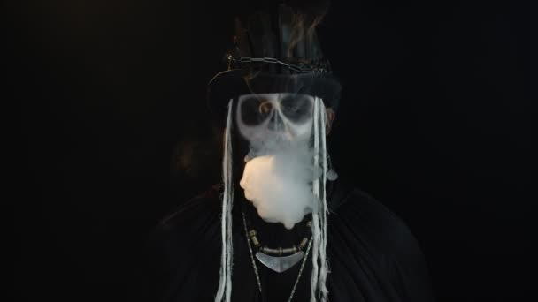 Gruseliger Mann mit Skelett-Make-up. Kerl atmet Zigarettenrauchen aus seinem Mund und zeigt in die Kamera — Stockvideo