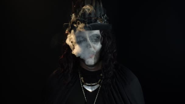 Sinister man with Halloween skeleton makeup exhaling cigarette smoking from his mouth and smiling — Stock Video