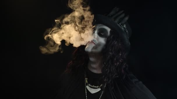 Hombre siniestro con maquillaje de cráneo profesional exhalando humo de cigarrillo de su boca y nariz — Vídeo de stock