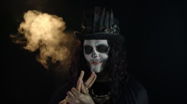 Şapkalı, iskelet makyajlı ürkütücü bir adam. Adam surat yapıyor, dişlek gülüyor. Cadılar Bayramı tematik partisi