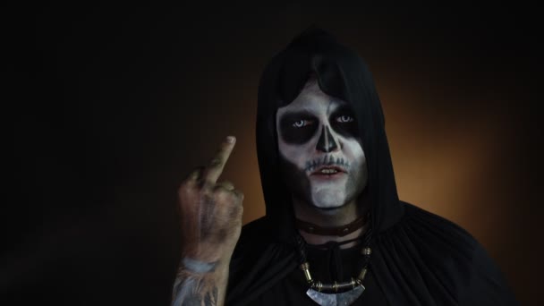 Finsterer Mann mit Totenkopf-Make-up, das Gesichter macht und Mittelfinger zeigt. Schlechte Geste. Halloween