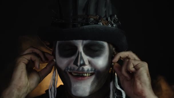 Złowieszczy człowiek z okropnym makijażem szkieletu Halloween zakłada słuchawki, zaczyna tańczyć, świętować — Wideo stockowe