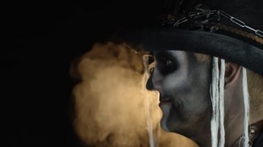 İskelet giymiş korkutucu bir adam Cadılar Bayramı makyajıyla başını çevirir ve gözleri açık kameraya bakar.