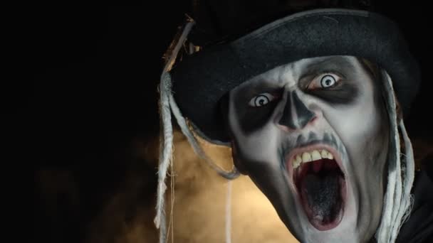 Aterrador hombre en esqueleto de Halloween maquillaje vuelve la cabeza y mira a la cámara con los ojos bien abiertos — Vídeos de Stock