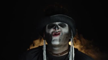 İskelet makyajlı uğursuz, deli bir adam. Kızgın suratlar yapan, başını sallayan, dilini gösteren bir adam.