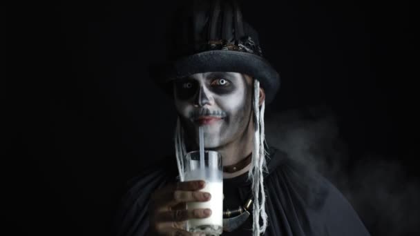 Gruseliger Typ im Karnevalskostüm von Halloween-Skelett blickt in die Kamera, trinkt Milch aus einem Glas — Stockvideo