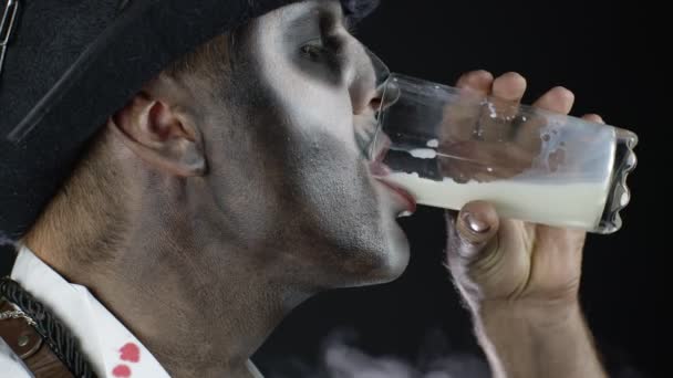 Gruseliger Mann mit Skelett-Make-up im weißen Hemd. Kerl schaut in die Kamera, trinkt Milch aus einem Glas — Stockvideo