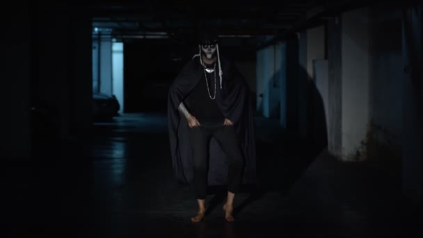 Creepy scary man in skeleton Halloween makeup dancing against dark parking hallway in slow motion — Stock Video