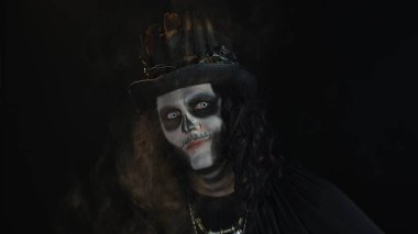 İskelet makyajlı ürkütücü bir adam. Adam başını çeviriyor ve kameraya bakıyor, korkutmaya çalışıyor.