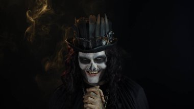 Şapkalı, iskelet makyajlı ürkütücü bir adam. Adam surat yapıyor, dişlek gülüyor. Cadılar Bayramı tematik partisi