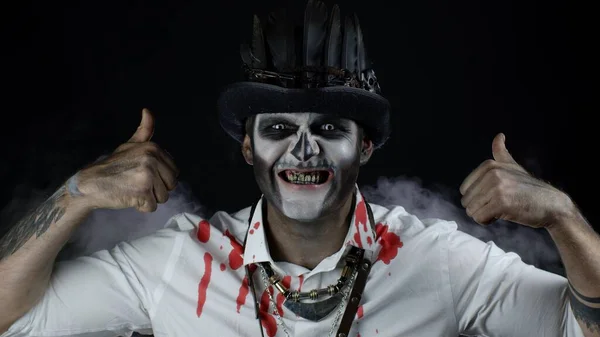 Een angstaanjagende glimlachende man in een Halloween kostuum met duimen omhoog gebaar. Zwarte achtergrond — Stockfoto