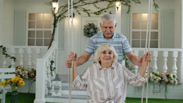 Pareja de ancianos juntos en el patio delantero en casa. Hombre balanceándose y abrazando a mujer. Feliz familia madura — Vídeos de Stock