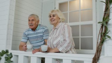 Yaşlı bir çift kahve içiyor, Coronavirus karantinası sırasında verandada kucaklaşıyorlar.