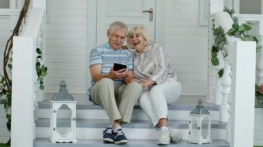Üst düzey çift evdeki verandada dijital tablet kullanıyor. Sosyal medya ağında komik videolar izlemek