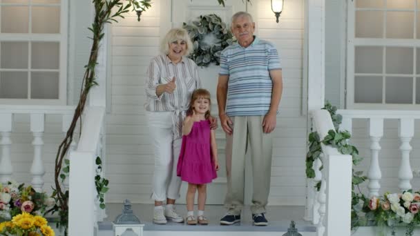 Ηλικιωμένοι παππούδες ζευγάρι με εγγονή στη βεράντα στο σπίτι κουνώντας το χέρι, δείχνοντας τους αντίχειρες επάνω — Αρχείο Βίντεο