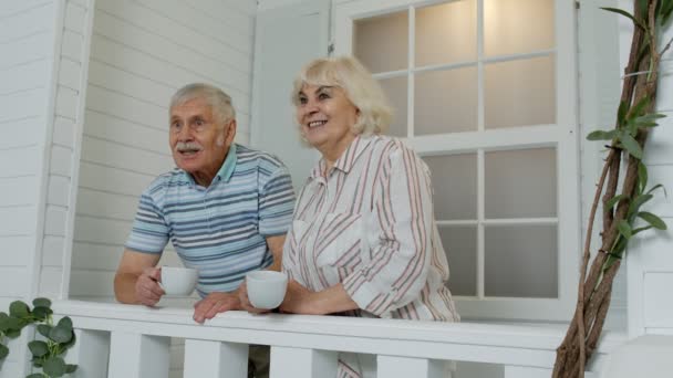 Pareja de ancianos mayores tomando café, abrazándose en el porche en casa durante la cuarentena del coronavirus — Vídeos de Stock