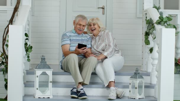 Старшая пара использует цифровой планшет в крыльце дома. Смотреть смешные видео в социальных сетях — стоковое видео