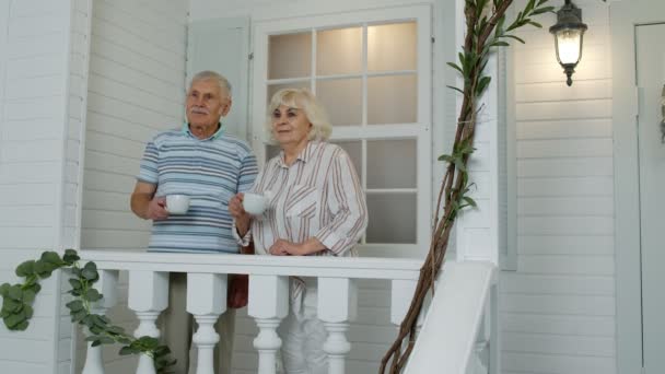 Mayores de edad pareja caucásica bebiendo café, mirando hacia el futuro en el porche en casa. Familia madura — Vídeos de Stock