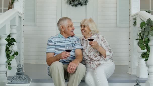 Mayores de edad pareja caucásica beber vino en el porche en casa, mirando a la cámara y sonriendo — Vídeos de Stock