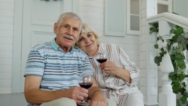 Ηλικιωμένο ζευγάρι που πίνει κρασί, αγκαλιάζεται στη βεράντα στο σπίτι κατά τη διάρκεια της καραντίνας του Coronavirus — Αρχείο Βίντεο