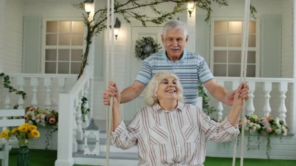 Evde ön bahçede kıdemli bir çift birlikte. Erkek, kadını sallıyor. Mutlu, olgun, emekli aile. — Stok video