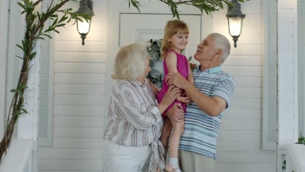 Happy senior grandfather and grandmother couple holding granddaughter in hands in porch at home — Stock Video