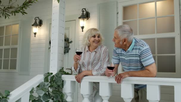 Idosos seniores casal caucasiano beber vinho na varanda em casa. feliz maduro aposentado família descansando — Vídeo de Stock