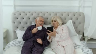 Pijama giyen yaşlı bir çift dijital tablete bakıp gülüyor ve eğleniyorlar.