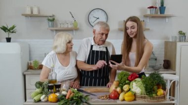 Sağlıklı besin tabletinin dijital tabletine sahip kızdan yemek tarifi dinleyen kıdemli erkek ve kadın.