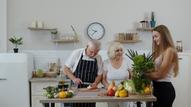 Oudere echtpaar in de keuken ontvangen groenten van kleindochter. Gezonde rauwe voeding — Stockvideo