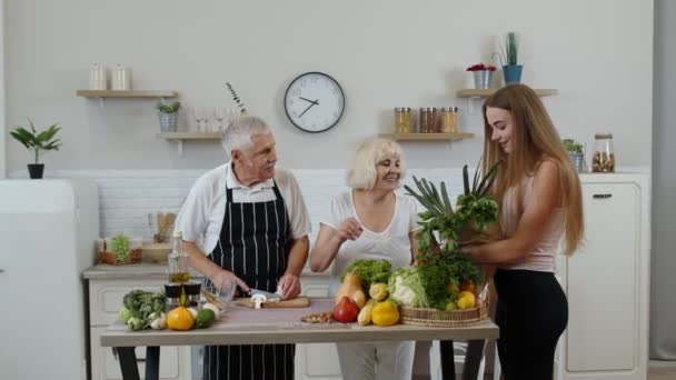 Пожилая пара на кухне получает овощи от внука. Сырая пища — стоковое видео