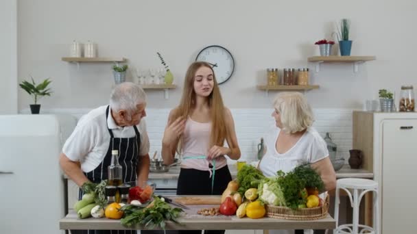 Chica que mide con cinta métrica su cintura delgada y braging delante de los abuelos. Dieta de alimentos crudos — Vídeo de stock