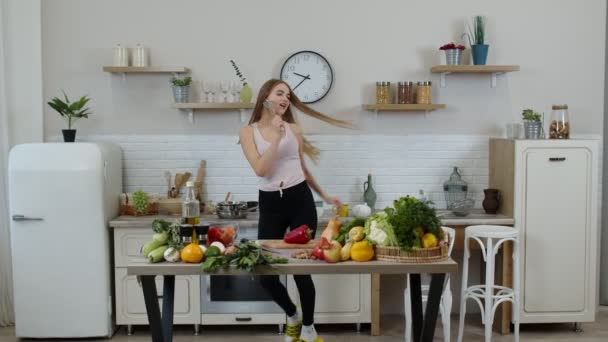 Preciosa chica vegana con el pelo largo bailando y cantando en la cocina moderna. Alimentación vegetal cruda dieta — Vídeos de Stock