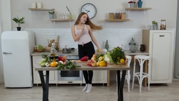 Gelukkig veganistisch meisje met slank taille dansen, zingen in de keuken. Rauwe plantaardige voeding dieet concept — Stockvideo