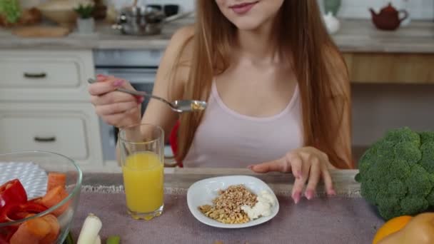 Chica encantadora comiendo brotes crudos de trigo sarraceno con nueces en la cocina con verduras y frutas frescas — Vídeo de stock