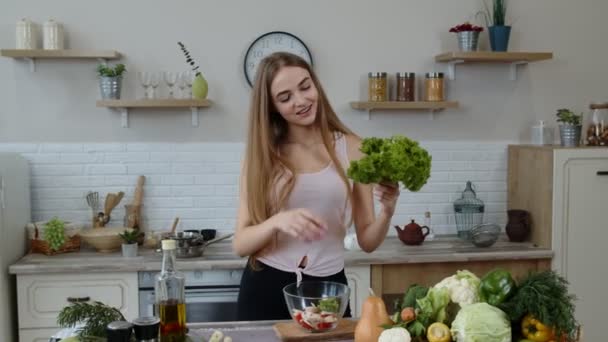 Chica joven bailando, divirtiéndose y cocinando ensalada con verduras crudas. Lanzar trozos de lechuga — Vídeos de Stock